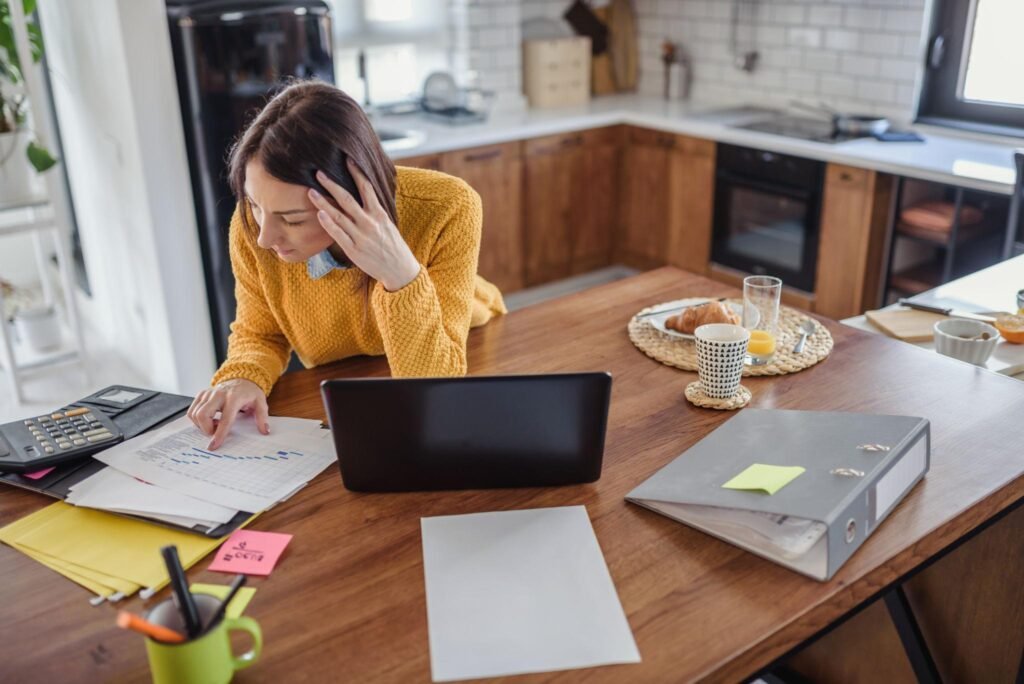 An overwhelmed woman managing work, planning, and household responsibilities at home.